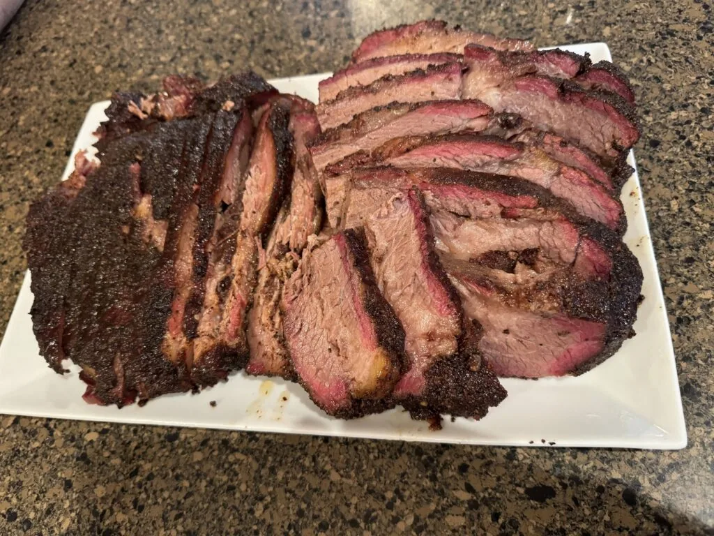 Sliced smoked brisket with dark bark and pink smoke ring arranged on white plate