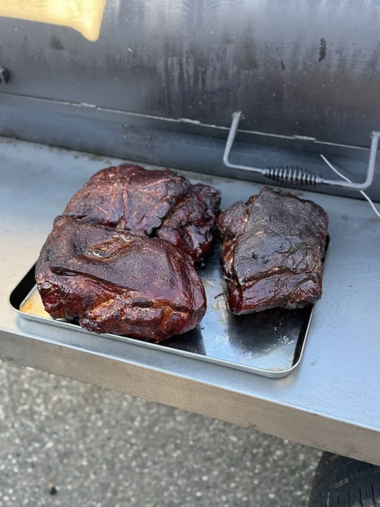 Three cooked beef steaks on a metal tray in a smoker with fogged glass door