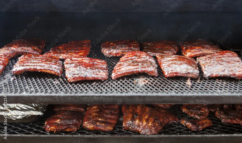 Multiple racks of ribs cooking on a smoker with smoke and caramelized glaze